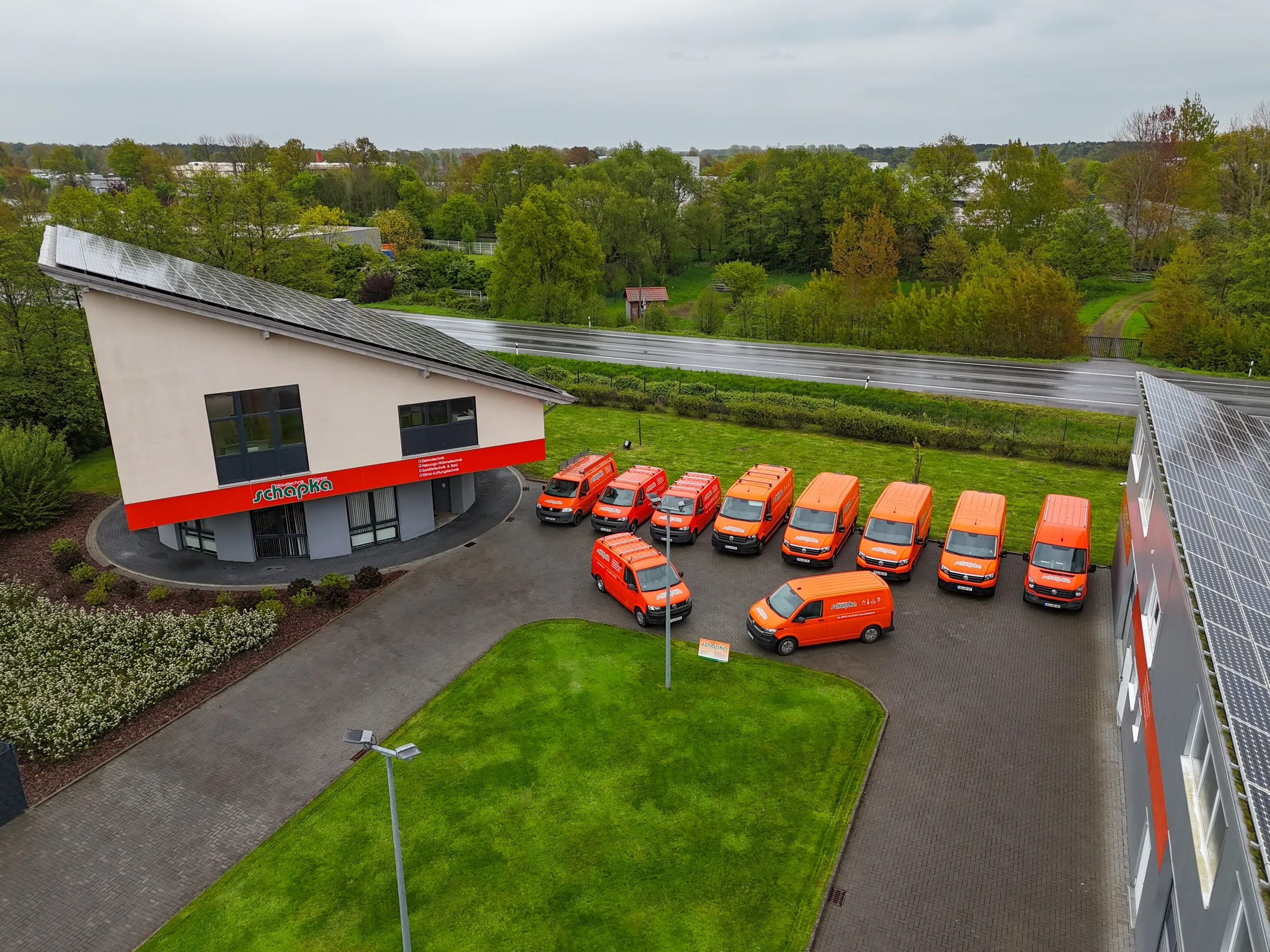 Firmensitz der Schapka GmbH in Espelkamp mit Photovoltaikdach und orangefarbener Kundendienstflotte